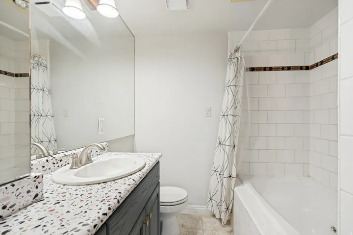 Bathroom featuring a white subway tile shower, a built-in tub, and a vanity with a terrazzo-style countertop
