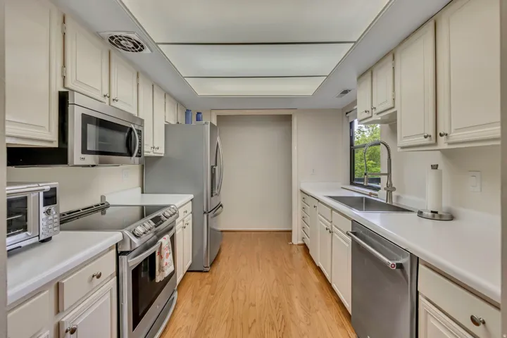 Kitchen featuring white cabinetry, white countertops, a stainless steel sink with a gooseneck faucet, a stainless steel appliances, and hard wood flooring