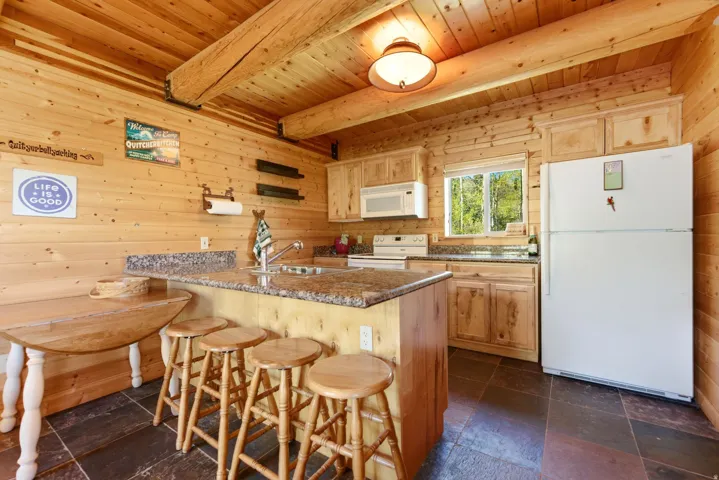 Kitchen featuring wood-paneled walls and ceiling, exposed wood beams, slate-style floor tiling, light wood cabinetry, and stone-finish countertops