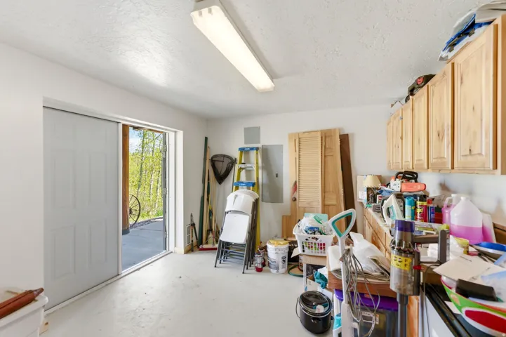 Utility room featuring painted concrete flooring, overhead fluorescent lighting, a sliding white panel door, and light wood cabinetry with upper storage