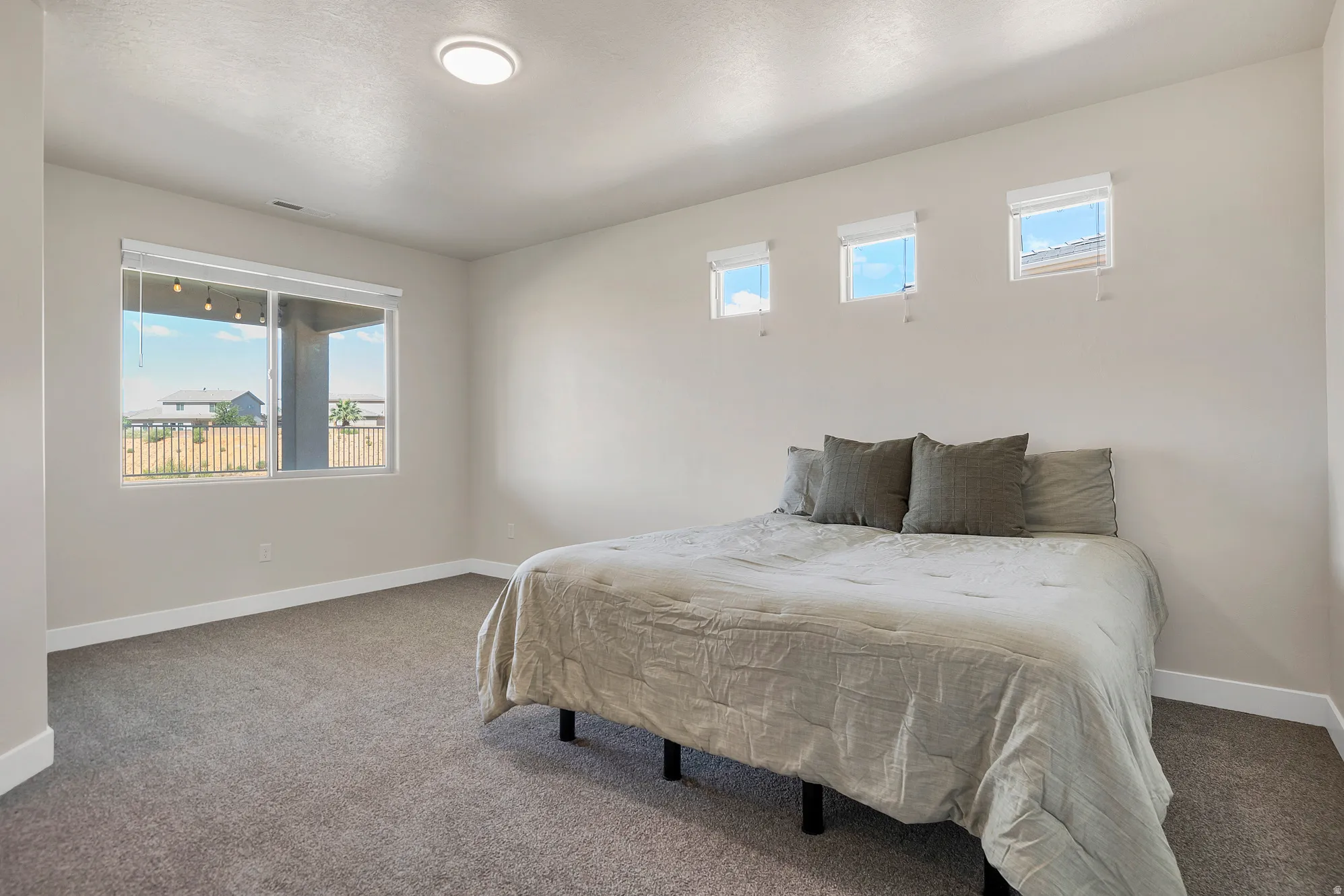 Carpeted room featuring a large sliding window, three upper windows with roller shades, white baseboards, and a flush-mount ceiling light