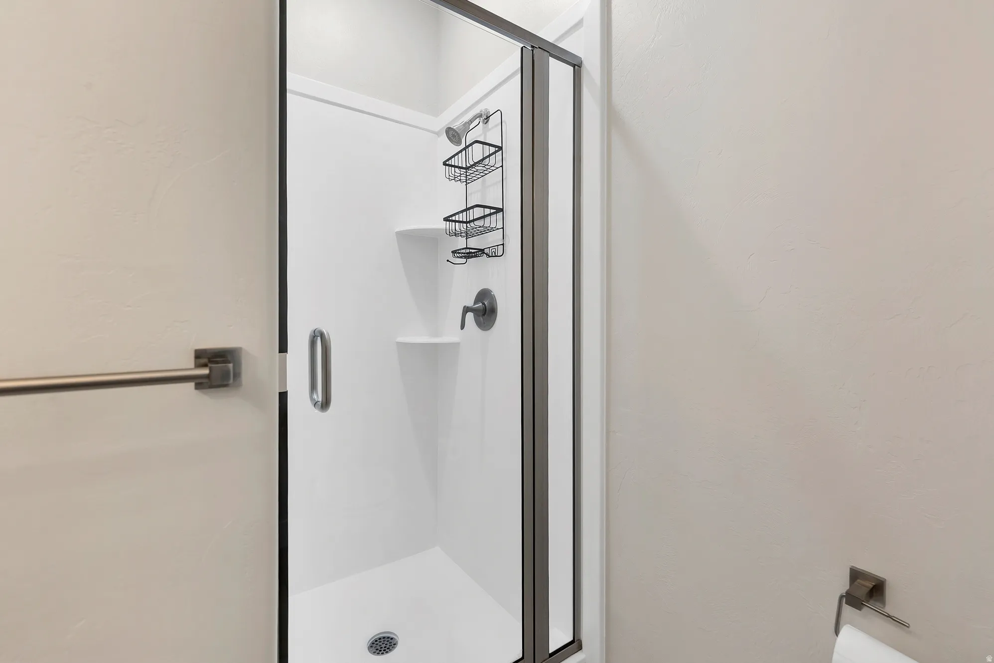 Shower enclosure featuring a white shower base and walls, a frameless glass door with a brushed nickel handle, and a wall-mounted showerhead with coordinating fixtures