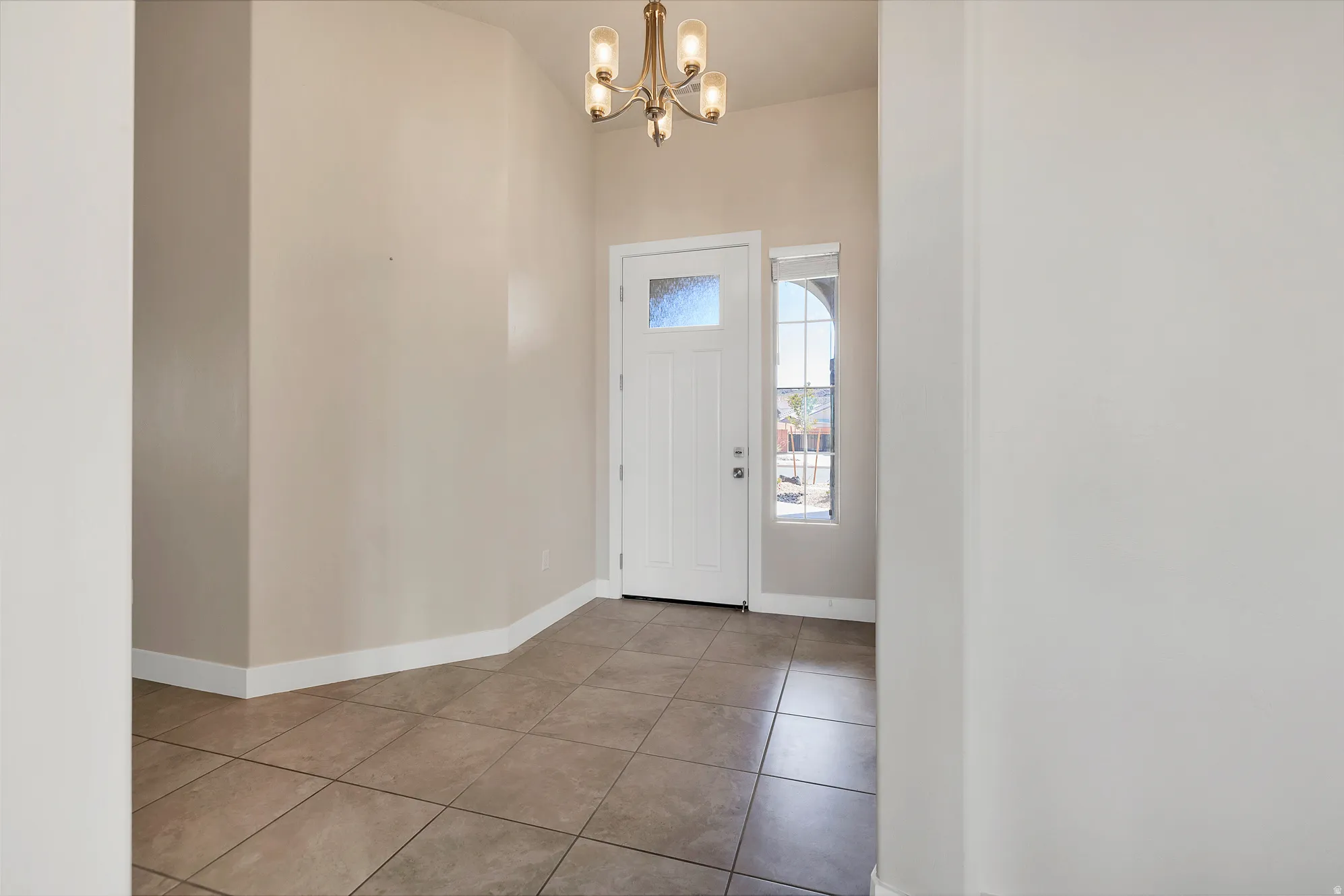 Entryway featuring a white paneled door with frosted glass, ceramic tile flooring, and a decorative chandelier