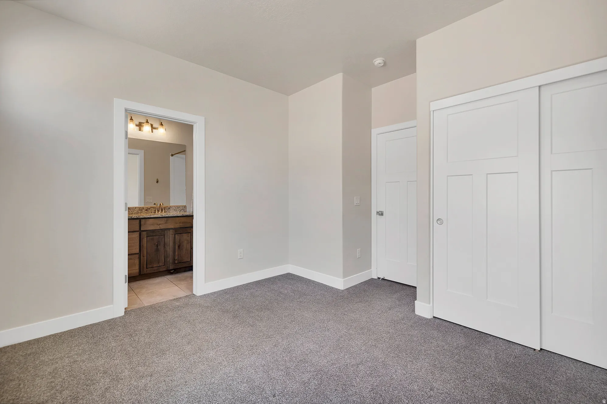 Bedroom featuring gray carpet flooring, white baseboards, and a doorway to a bathroom