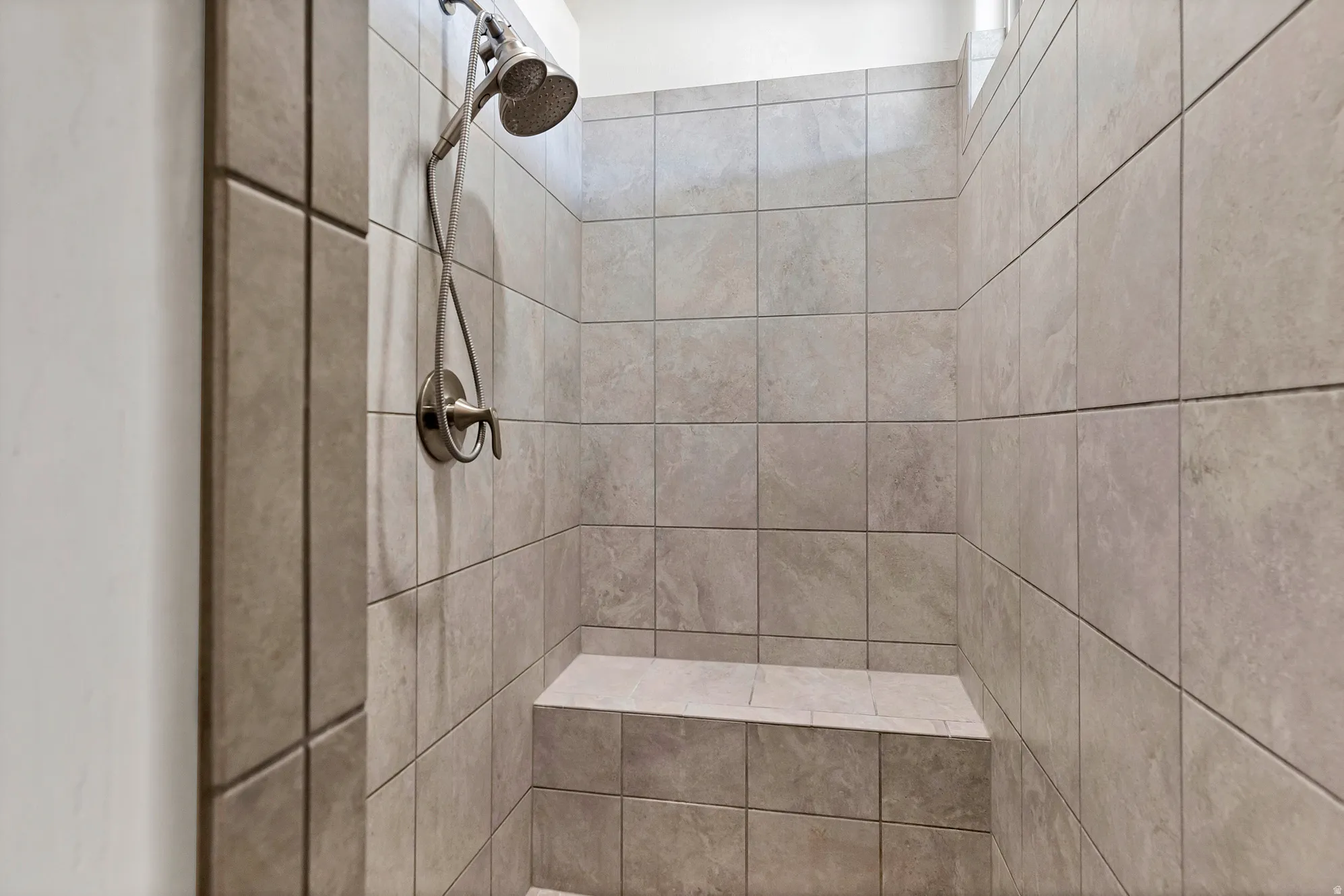 Tiled shower with a built-in bench, brushed nickel shower head, and an adjustable handheld shower sprayer