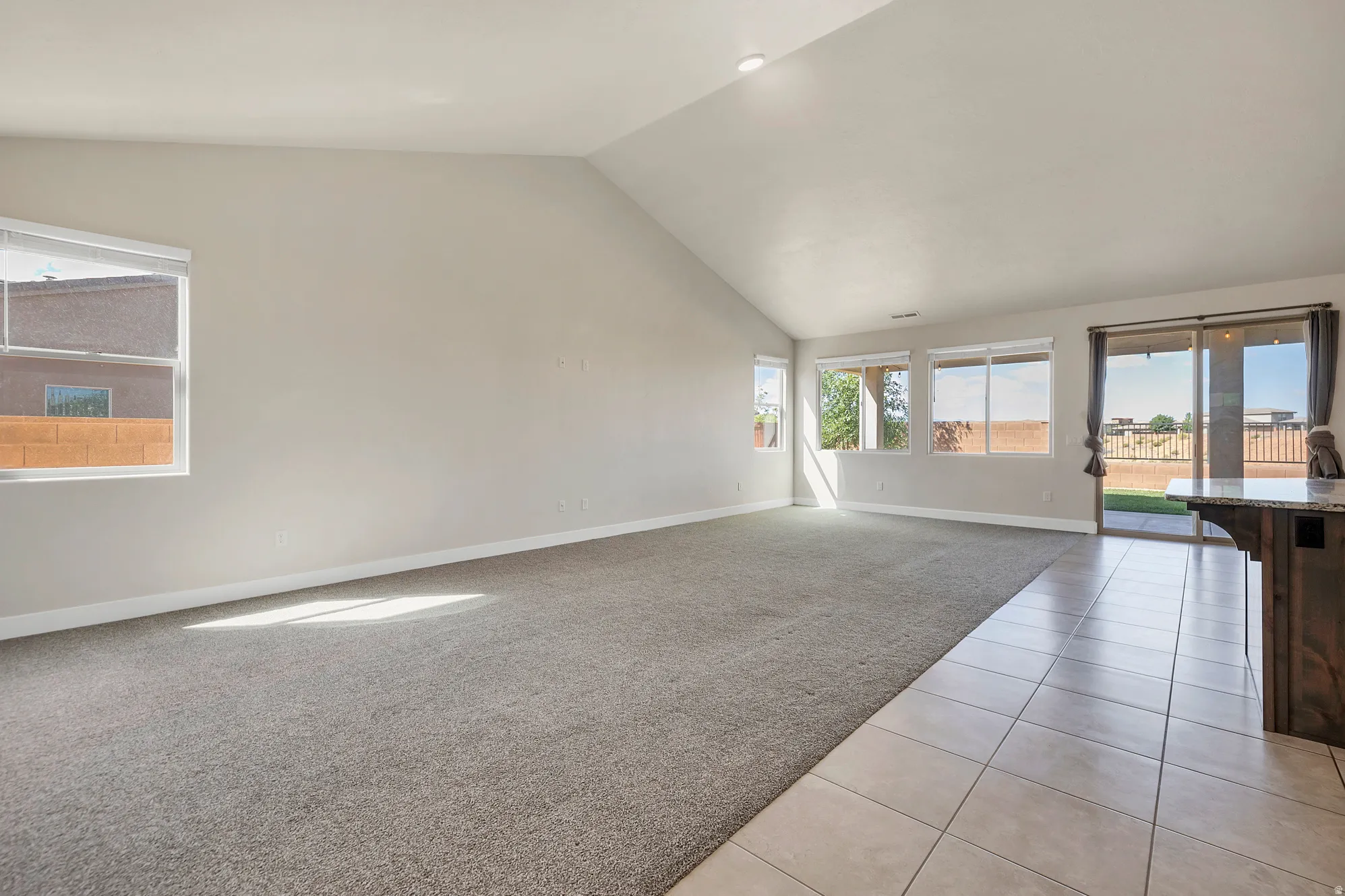 Open concept living area featuring vaulted ceilings and a combination of carpet and tile flooring