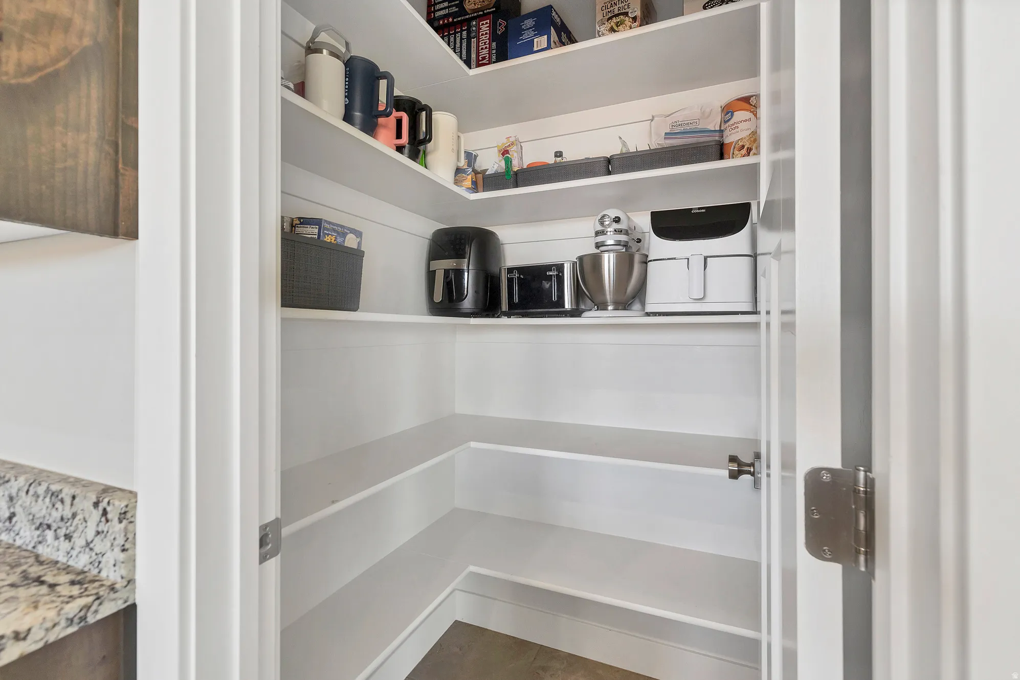 Spacious pantry featuring multiple white shelves, a corner configuration, and ample storage capacity