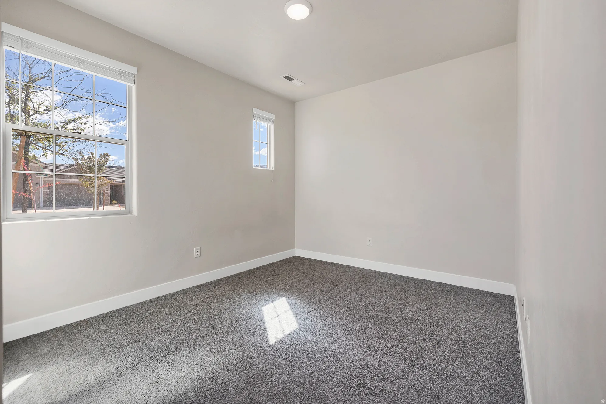 Room featuring a large window with white blinds, a smaller secondary window, light gray wall paint, dark gray carpeting, and white baseboards