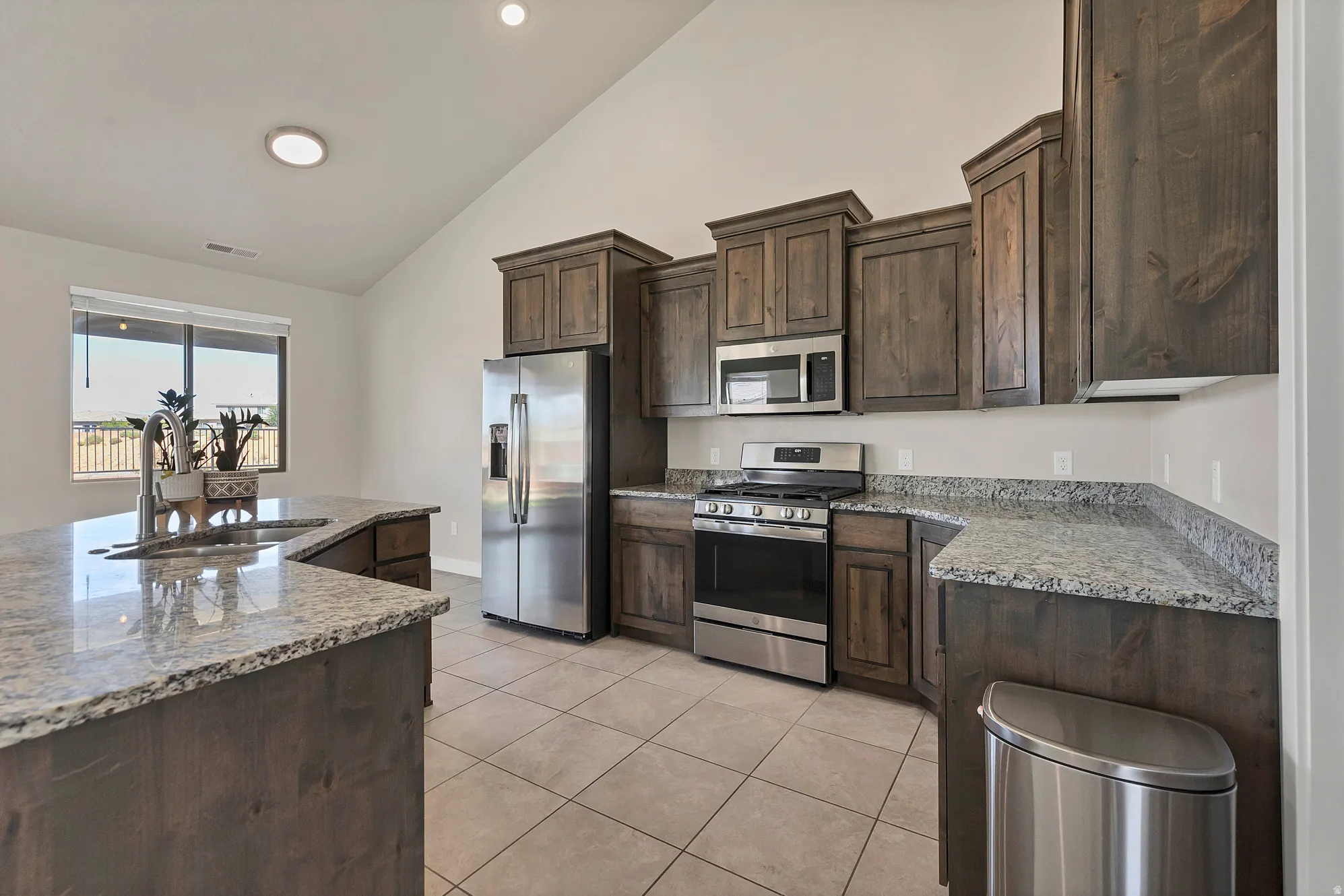 Kitchen featuring wood-finish cabinetry, granite countertops, and stainless steel appliances including a refrigerator, range, and microwave
