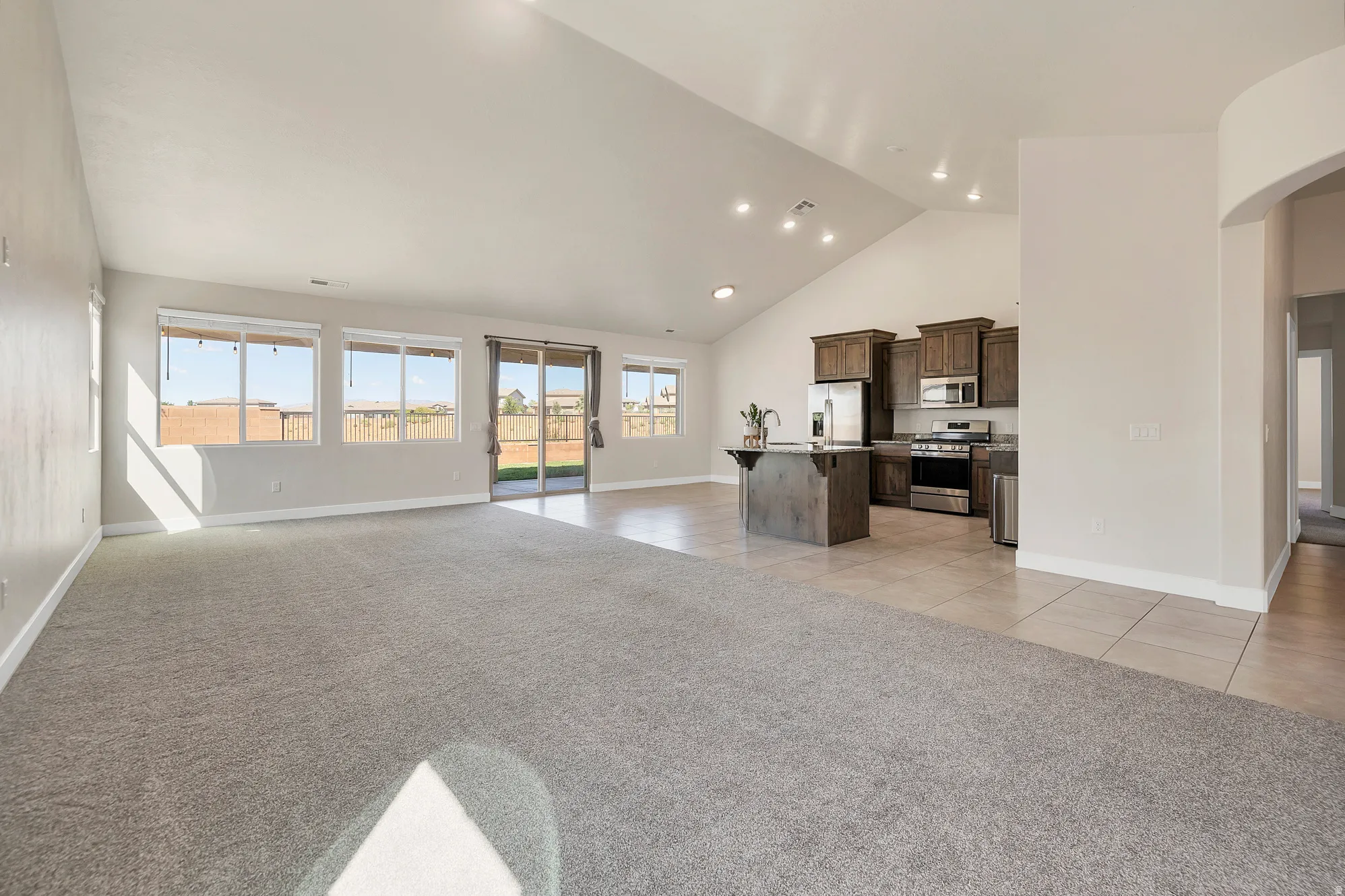 Spacious open-concept living area featuring vaulted ceilings, recessed lighting, and a blend of carpeting and tile flooring