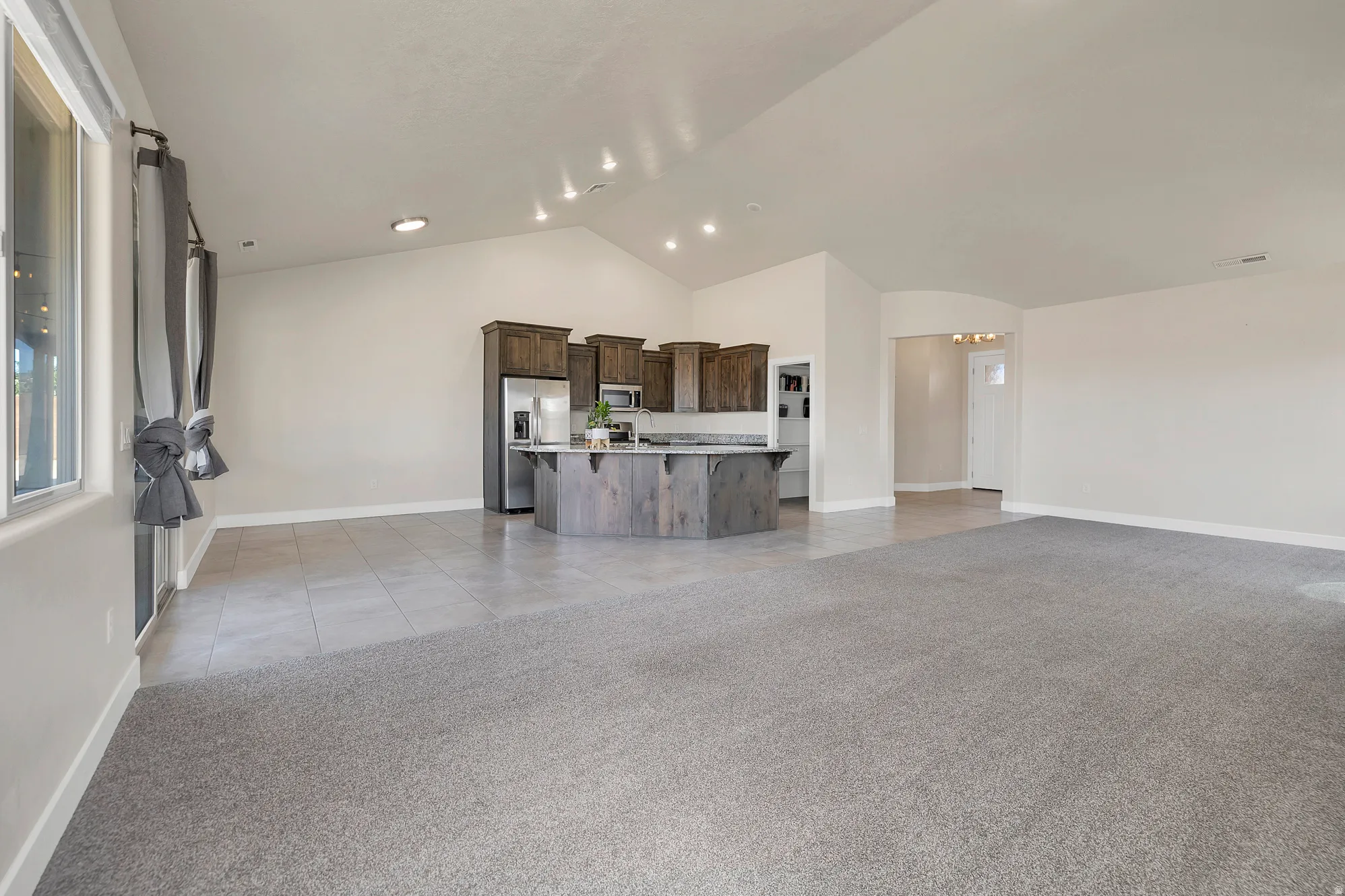 Open-concept living area featuring vaulted ceilings, recessed lighting, and a kitchen with wood-finish cabinetry, stainless steel appliances, and an island with a countertop
