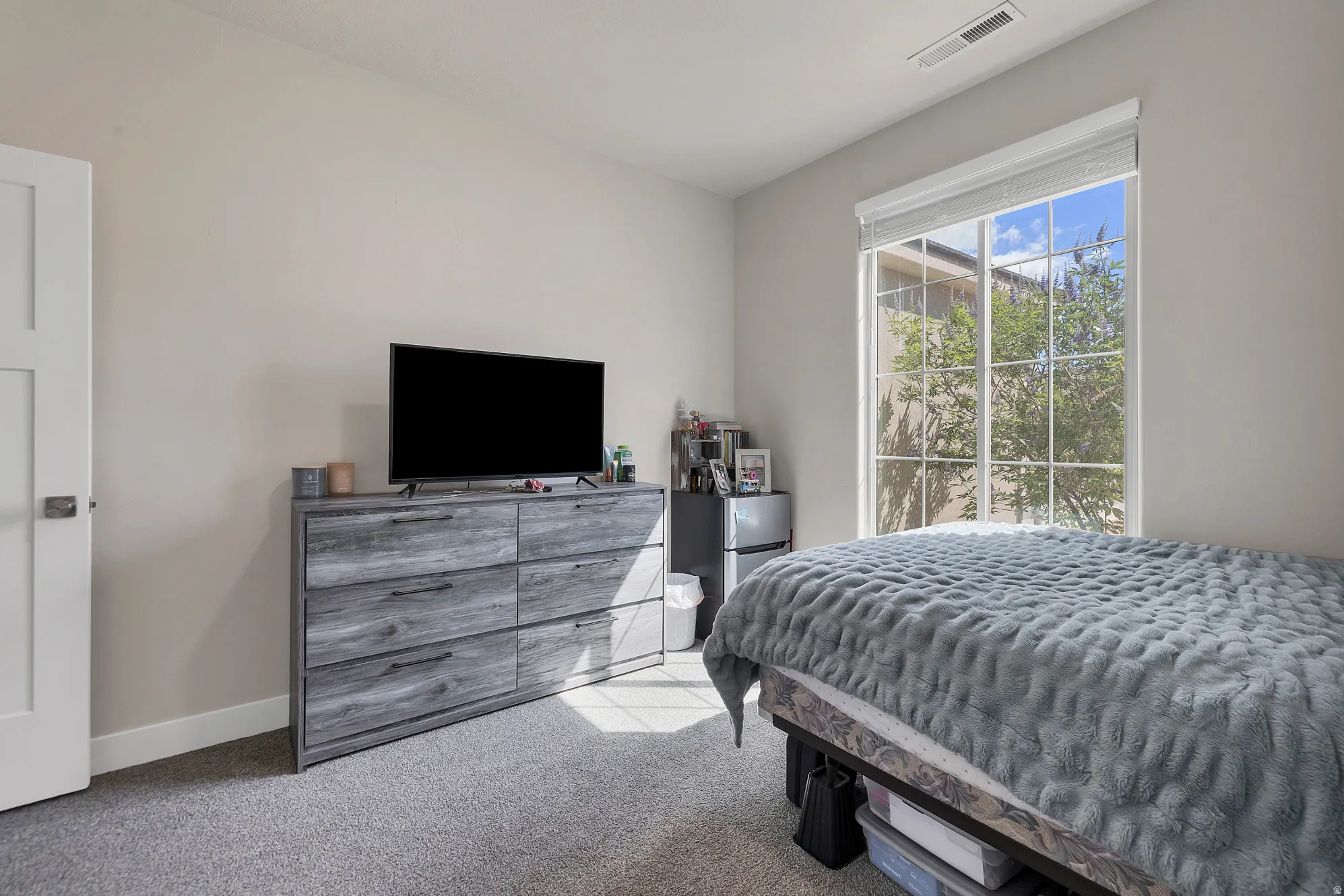Bedroom featuring neutral tone walls, gray carpet, a white paneled door, and a large window with grid panes