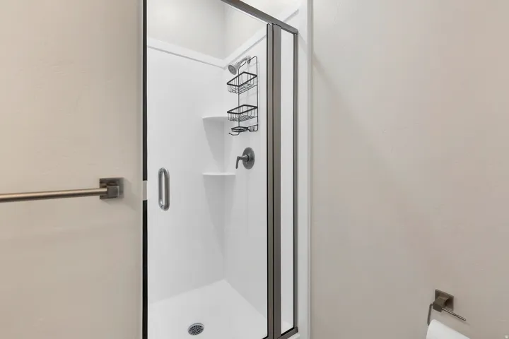 Shower enclosure featuring a white shower base and walls, a frameless glass door with a brushed nickel handle, and a wall-mounted showerhead with coordinating fixtures