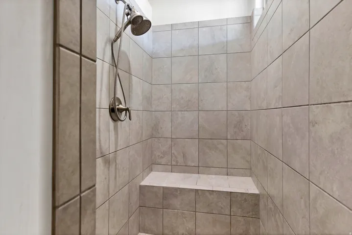 Tiled shower with a built-in bench, brushed nickel shower head, and an adjustable handheld shower sprayer