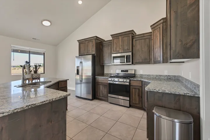 Kitchen featuring wood-finish cabinetry, granite countertops, and stainless steel appliances including a refrigerator, range, and microwave