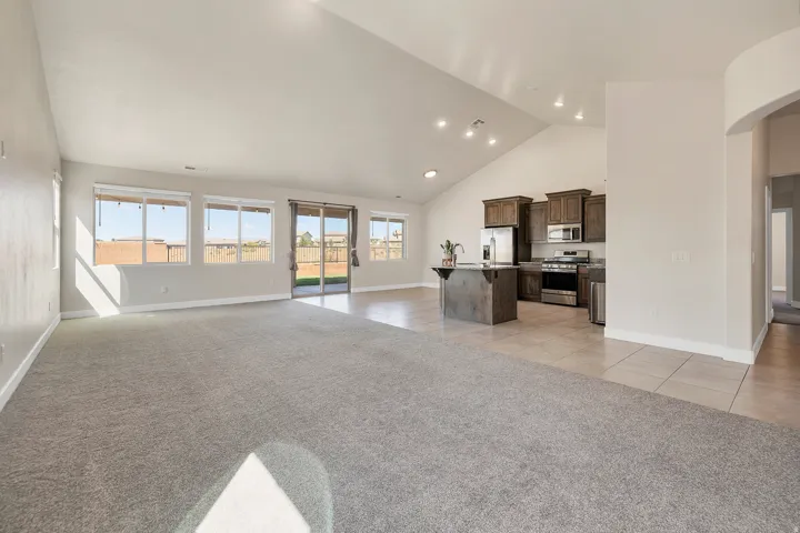Spacious open-concept living area featuring vaulted ceilings, recessed lighting, and a blend of carpeting and tile flooring