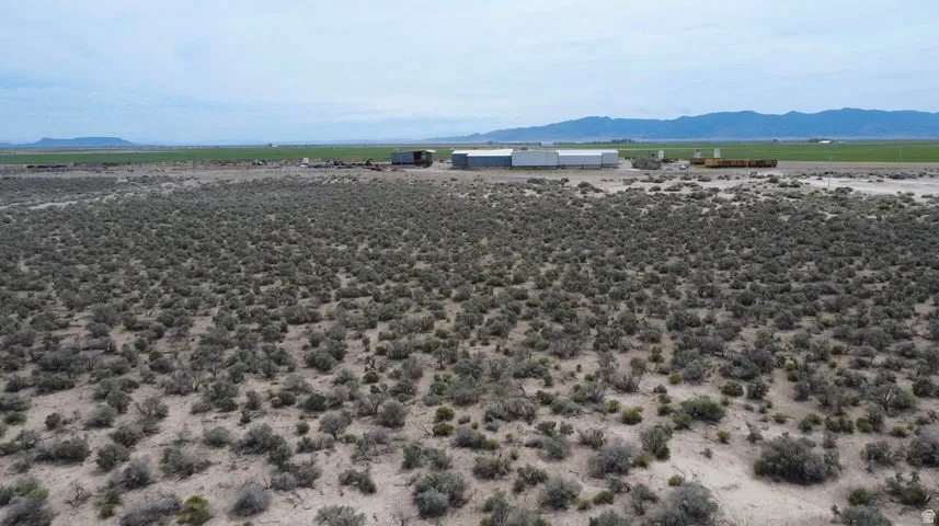 Expansive arid landscape with native vegetation, featuring distant agricultural fields and mountains