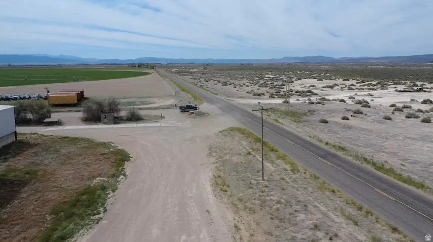 Expansive rural landscape featuring a paved road, arid terrain with scattered vegetation, and distant agricultural fields