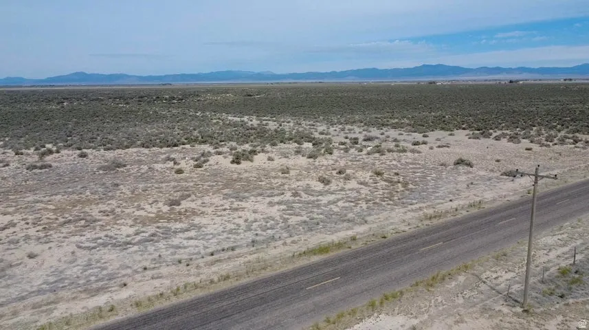 Expansive desert landscape featuring a paved road, scattered vegetation, and distant mountain ranges