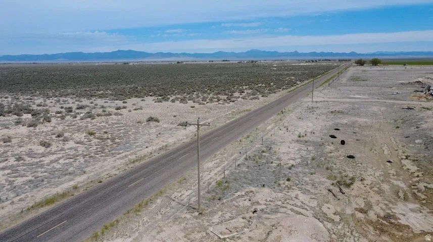 Expansive undeveloped land featuring a paved road, utility poles, and distant mountain ranges