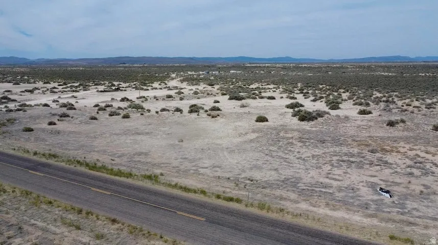 Expansive desert landscape featuring a paved road, scattered vegetation, and distant mountains under a cloudy sky