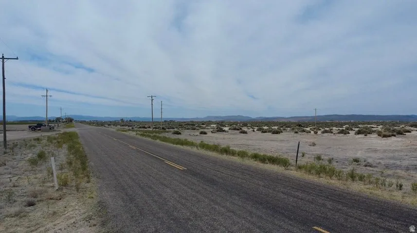 Expansive undeveloped land with a paved road frontage, utility poles, and distant mountain range