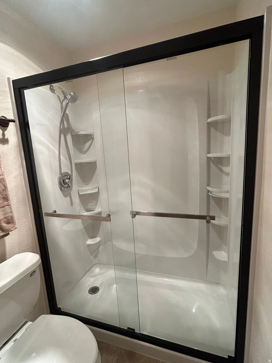 Shower enclosure featuring sliding glass doors with dark framing, an integrated shower system with a handheld sprayer, built-in shelving, and a white basin