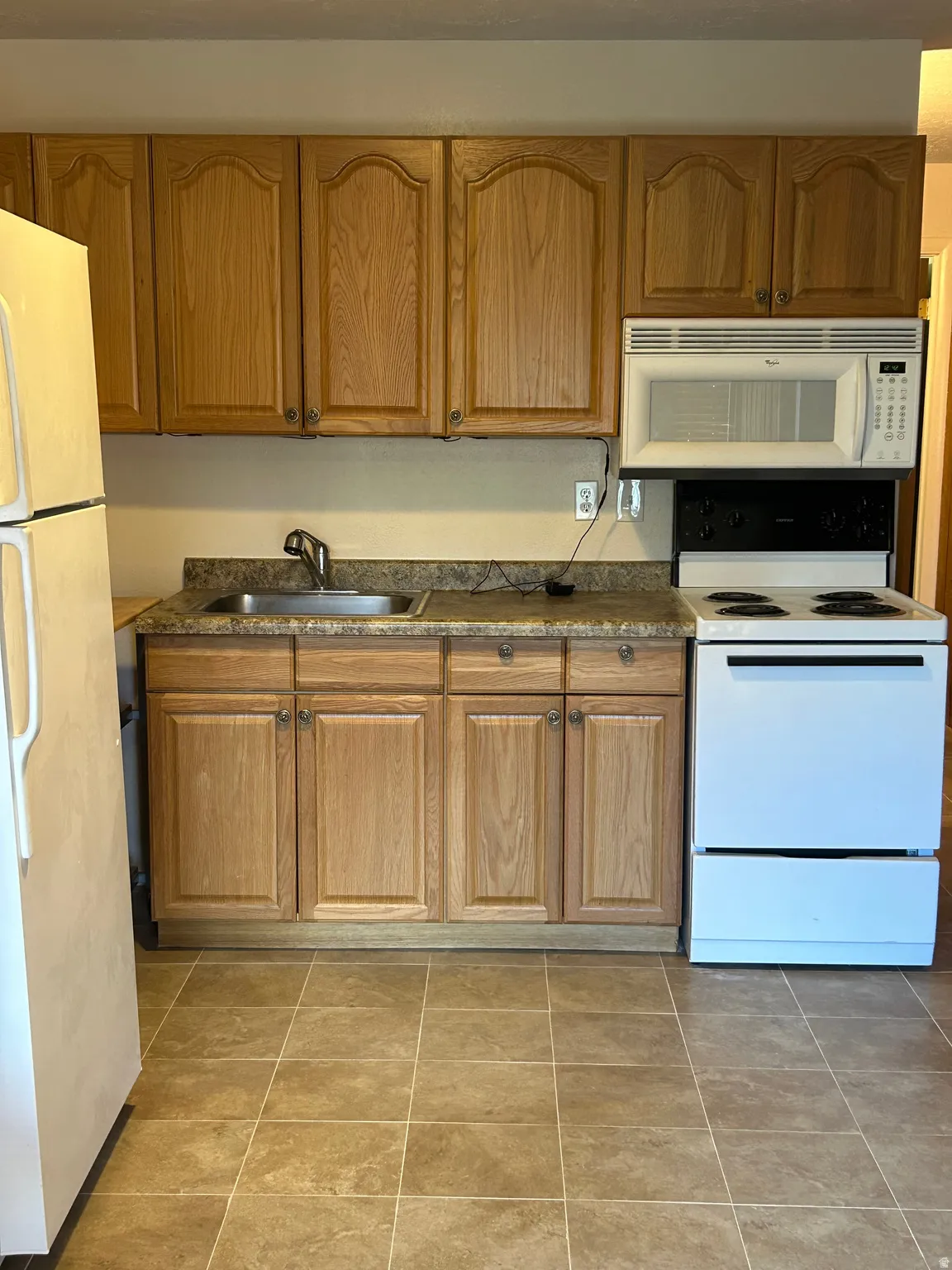 Kitchen featuring wood-finish cabinetry, a stainless steel sink, a microwave, and a white electric range
