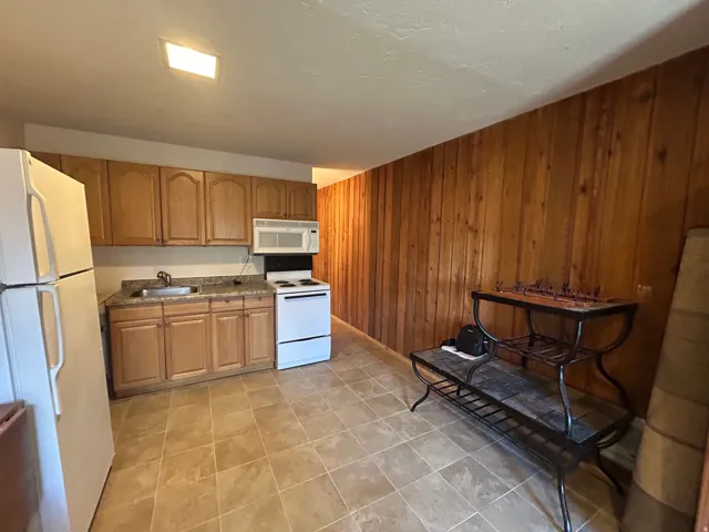 Kitchenette featuring light wood-finish cabinetry, a stone-look countertop, and a stainless steel sink with a chrome faucet