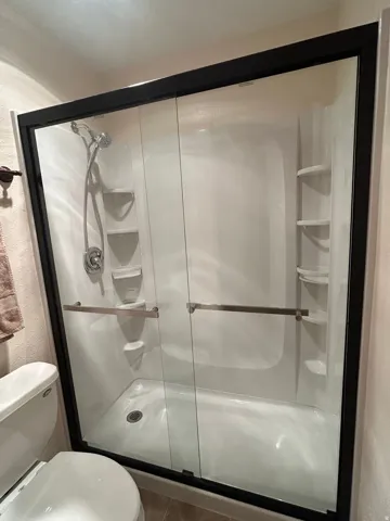 Shower enclosure featuring sliding glass doors with dark framing, an integrated shower system with a handheld sprayer, built-in shelving, and a white basin