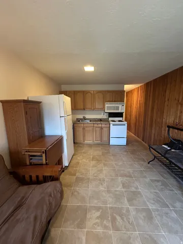 Kitchenette with wood-finish cabinetry, white appliances, and granite-look countertops