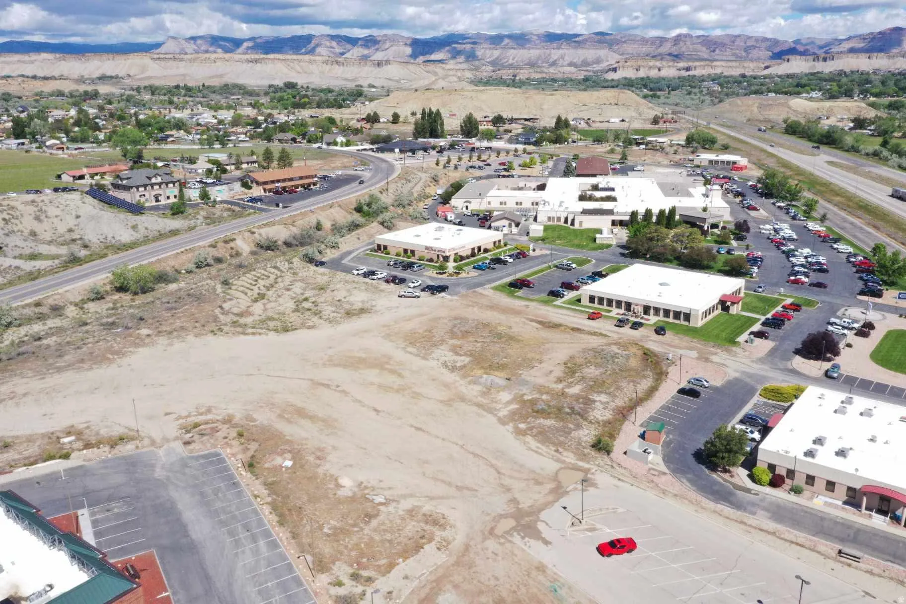 Expansive undeveloped land parcel featuring a relatively flat topography, surrounding commercial structures, and distant mountainous scenery