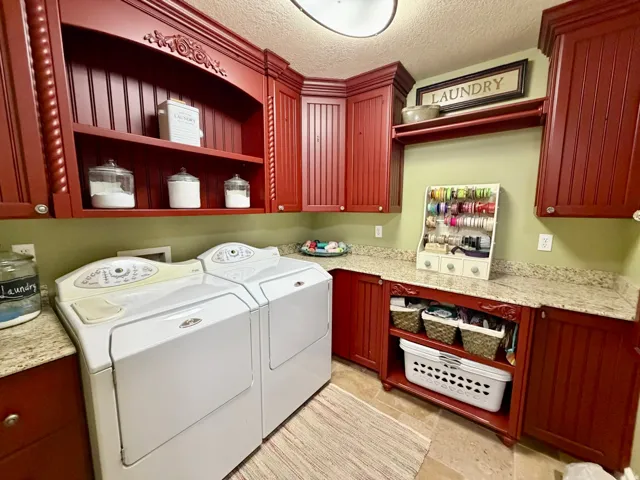 Laundry area featuring extensive red-stained cabinetry with carved details, an open display shelf, and granite-finish countertops
