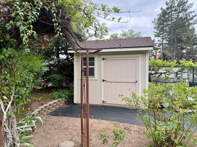 Utility shed with beige siding, a brown shingle roof, and a single window