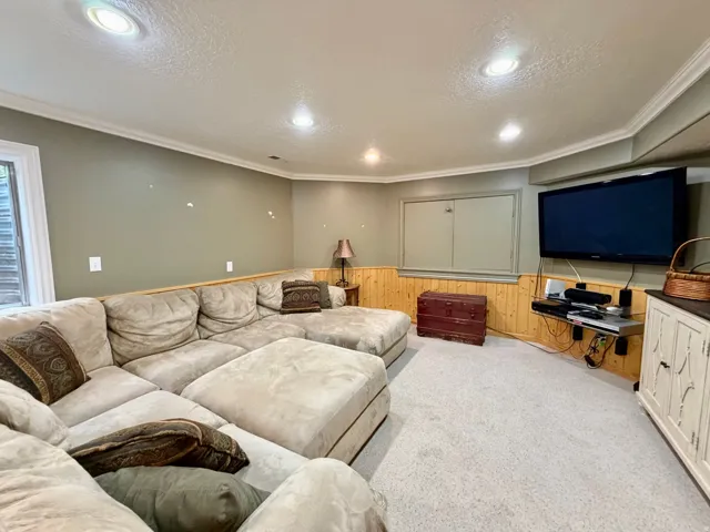 Recessed lighting illuminates this carpeted room featuring painted walls with wood paneling and crown molding