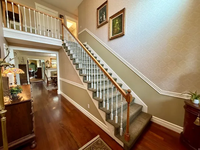 Two-story foyer featuring dark wood-finish flooring, a grand staircase with carpeted treads, white balusters, and a natural wood handrail