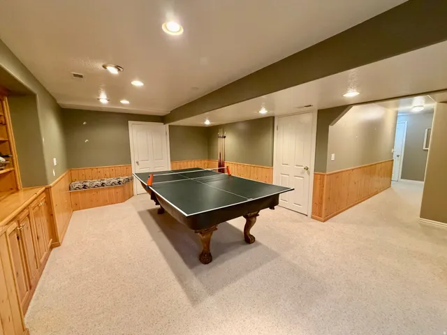Spacious recreation room featuring a ping-pong table, recessed lighting, wall-to-wall carpeting, wood-paneled wainscoting, and built-in cabinetry with shelving