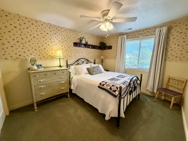 Carpeted room featuring a ceiling fan with integrated lighting, a window with blinds and drapes, and wainscoting with patterned wallpaper above