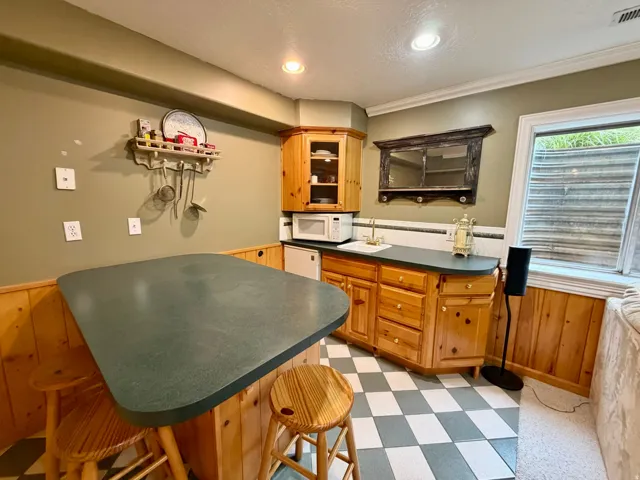 Functional kitchenette featuring wood-finish cabinetry, a sink with brass-finish faucet, and a black and white checkerboard floor