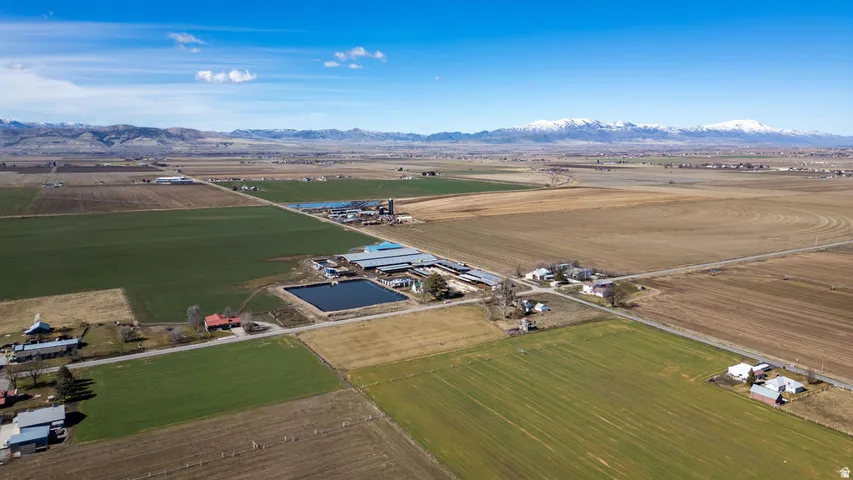 Expansive agricultural land featuring cultivated fields, farm buildings, and a large water reservoir, set against a backdrop of distant mountains