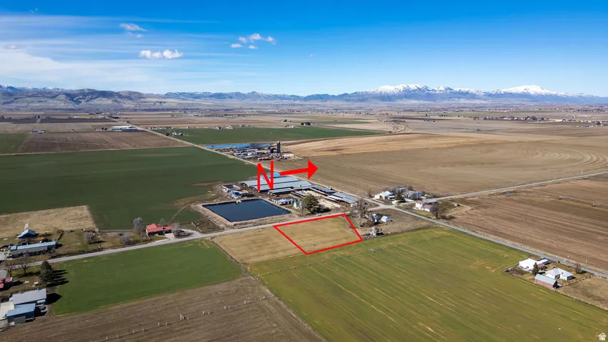 Expansive agricultural land parcel with clear boundaries, bordering a farm operation featuring multiple structures and a pond