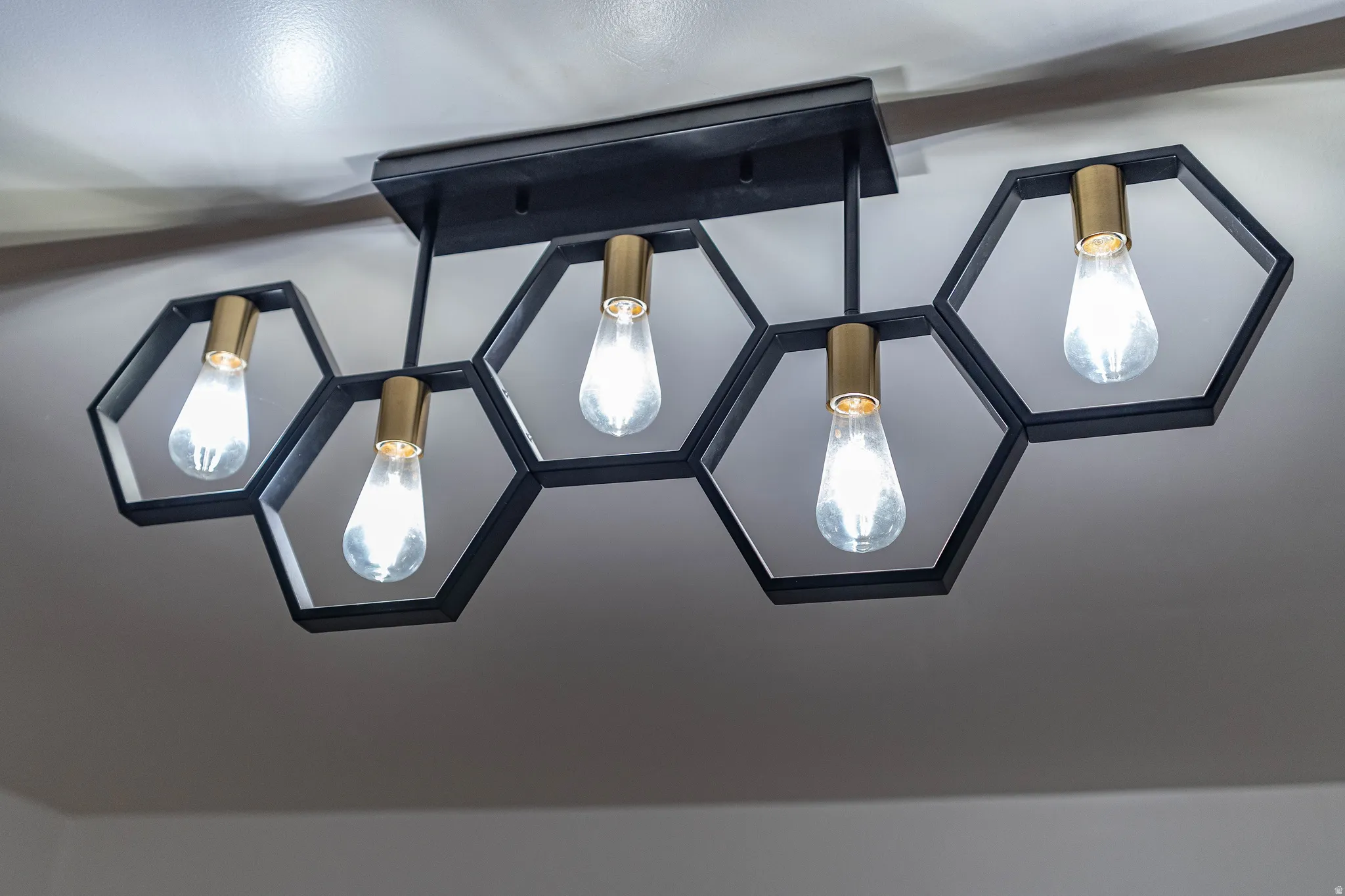 Ceiling-mounted light fixture featuring five hexagonal frames in matte black, each housing an Edison-style bulb with a brass-finish socket