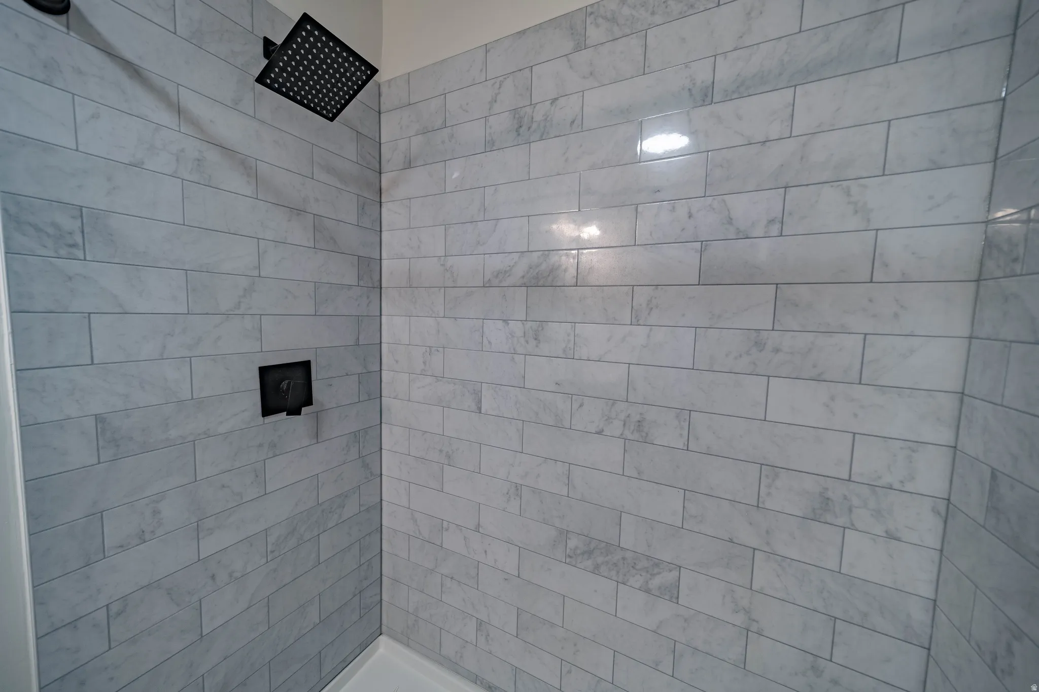 Shower featuring light-toned rectangular tile surround, a matte black rainfall showerhead, and a matte black wall-mounted control fixture
