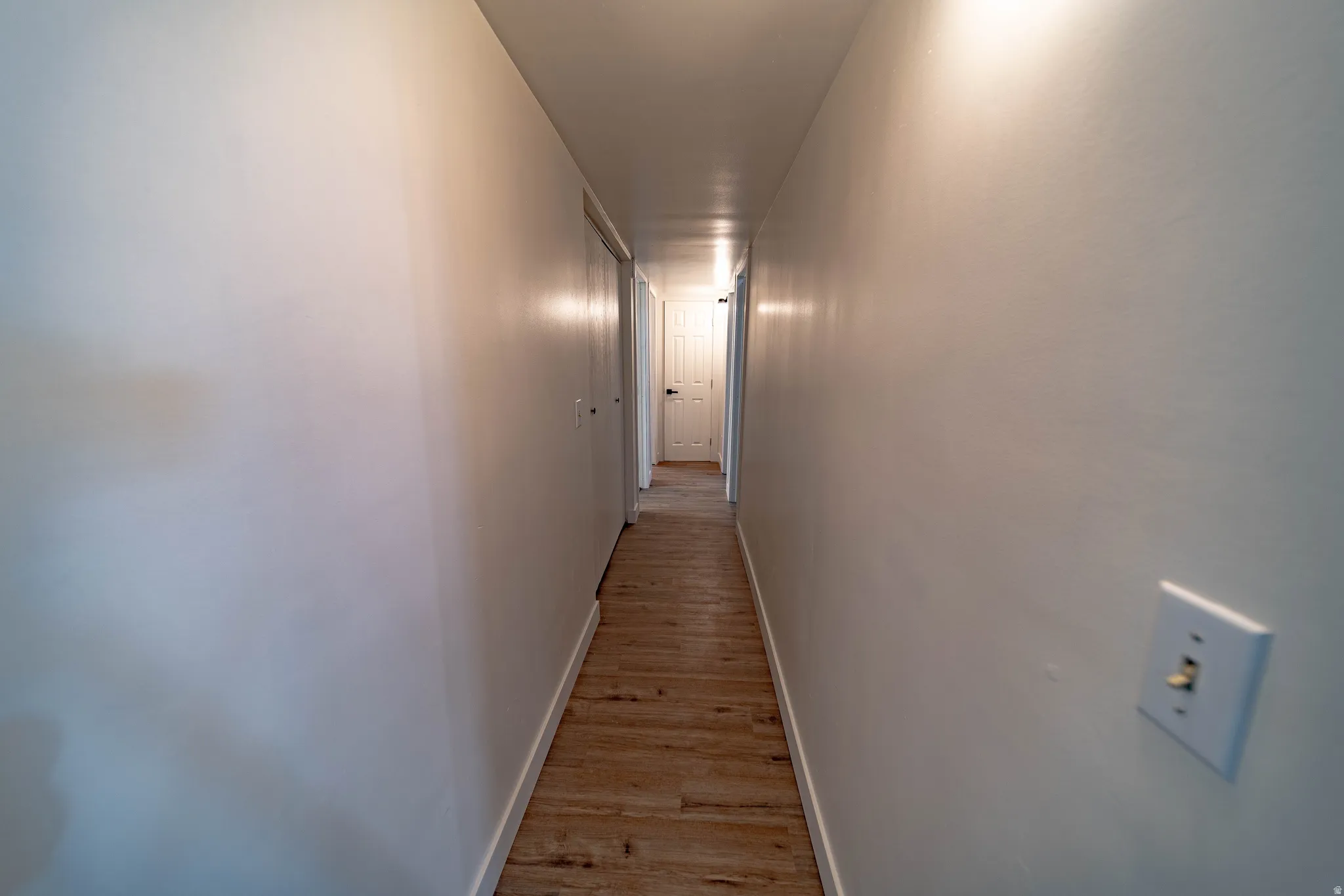 Hallway with wood-finish flooring, white walls, and white baseboards