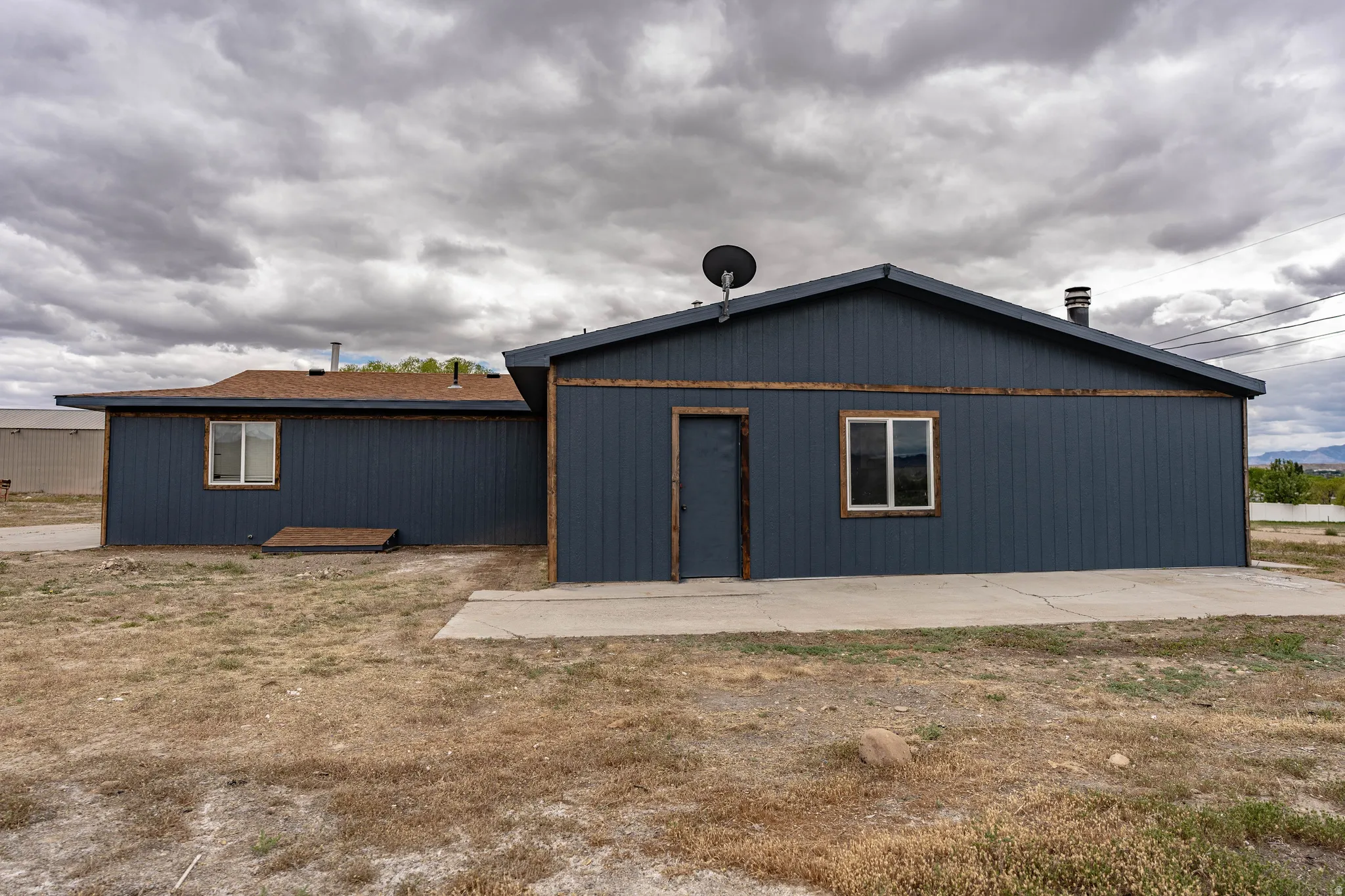 Dark blue vertical siding exterior with natural wood trim accents, multiple windows, and a concrete patio