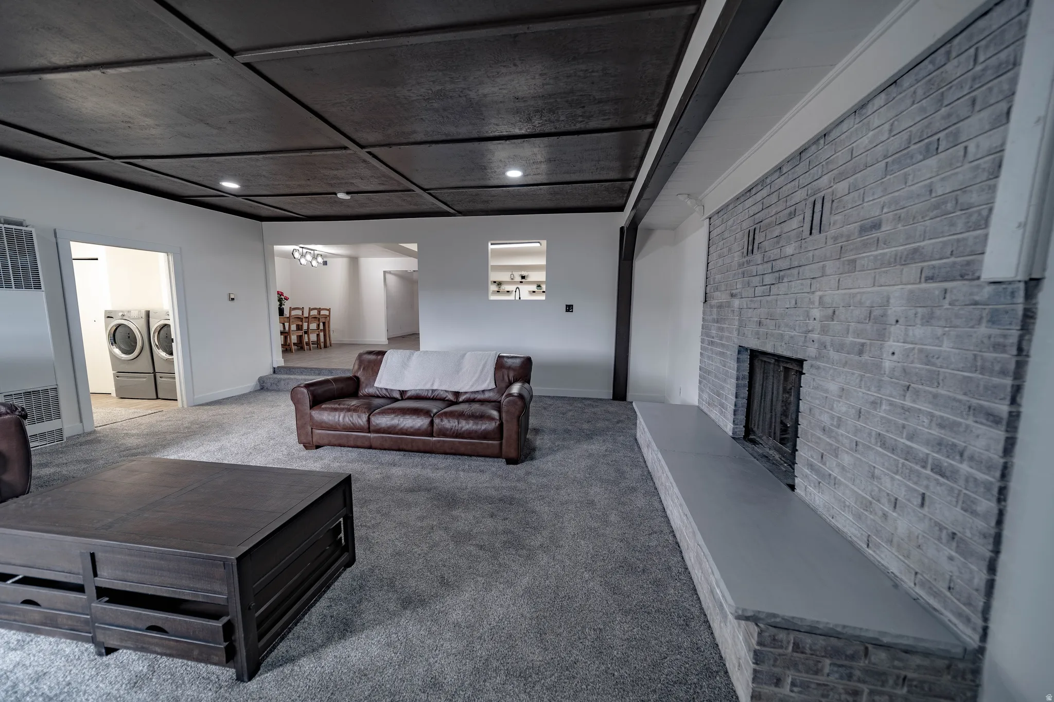 Inviting living area featuring a prominent brick fireplace with a stone hearth, coffered ceiling, recessed lighting, and soft carpeting