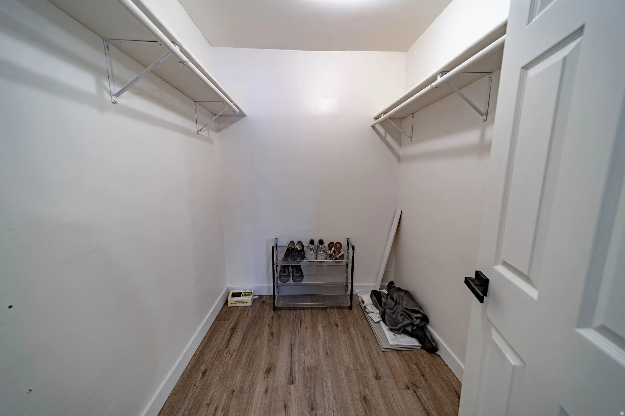 Spacious closet featuring wood-finish flooring, white baseboards, and two levels of built-in shelving with hanging rods