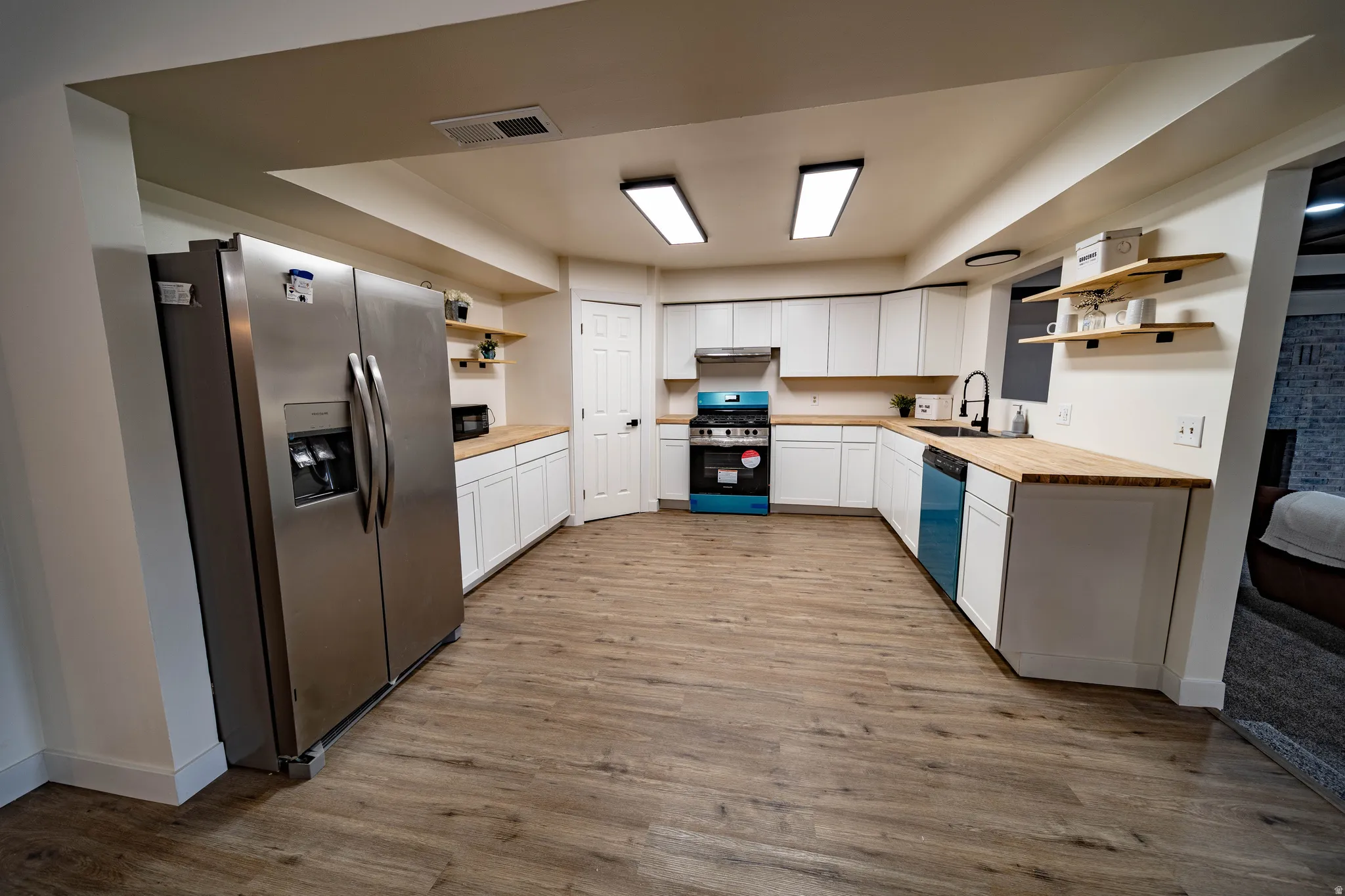 Spacious kitchen featuring wood-finish flooring, white cabinetry, butcher block countertops, and stainless steel appliances