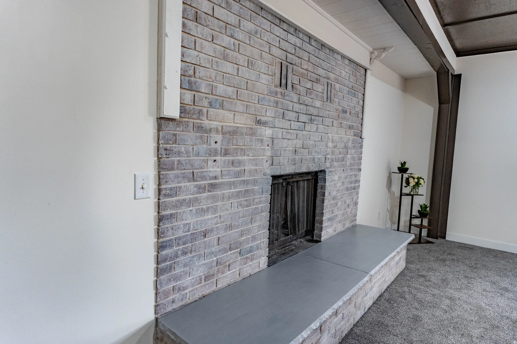 Exposed brick fireplace with a hearth, white painted walls, and textured carpeting