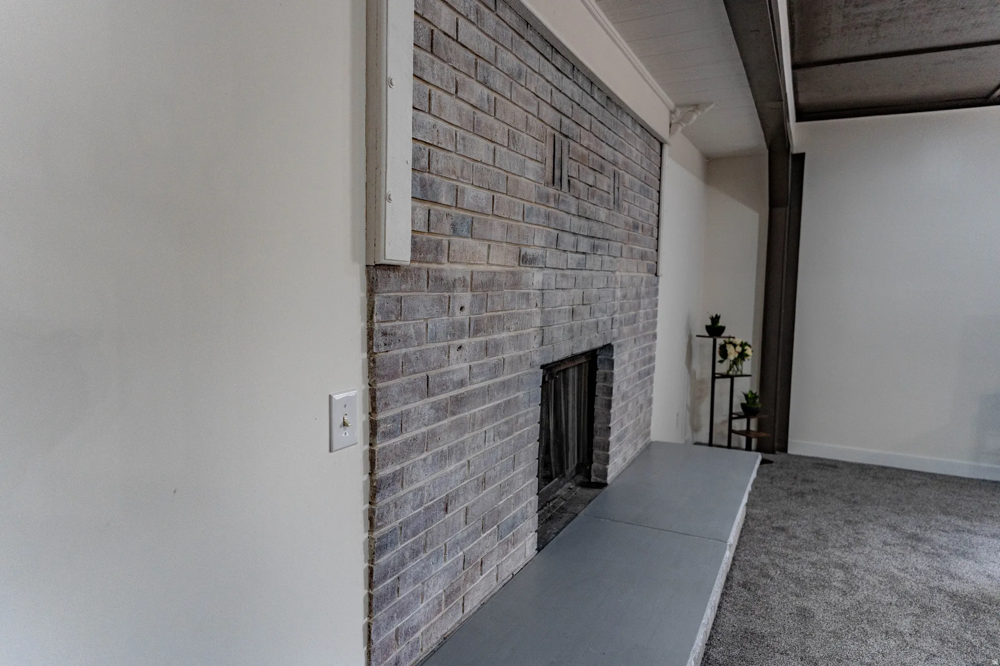 Brick fireplace with a stone hearth, white walls, and carpet flooring